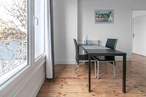 A room with a dining table, chairs, a radiator, and a window with a view of trees.