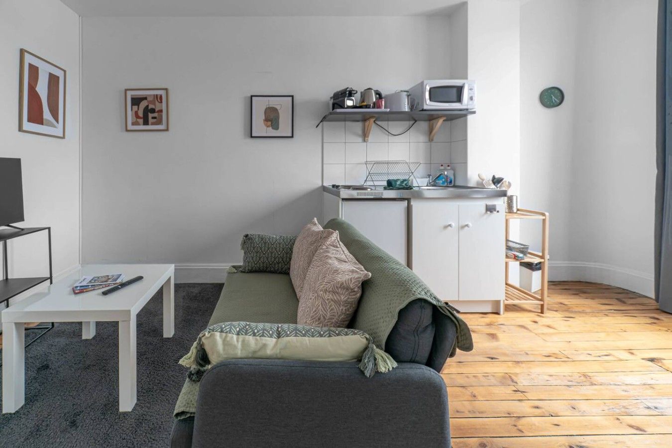 Un espace de vie compact comprenant un canapé, une petite table, un coin cuisine et un téléviseur.