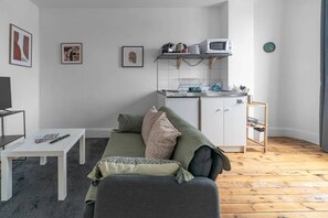 A compact living space with a sofa, a small table, a kitchenette, and a television. - Appartement design en centre ville (Vichy)