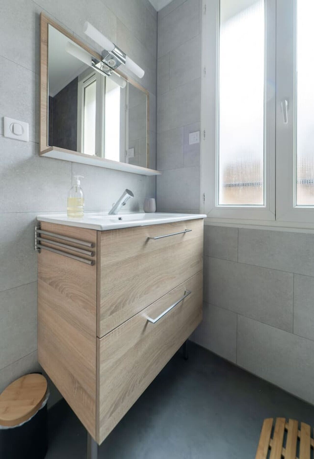 Un baño moderno con tocador de madera, un espejo y una ventana.