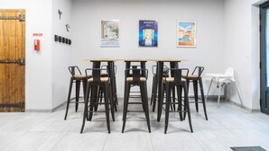 Un salón de conferencias con una mesa de madera y seis sillas negras con asientos de madera. Hay tres carteles en la pared, un detector de incendios y una puerta con un panel de madera.