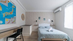 Un dormitorio con cama, escritorio y silla. Hay un mapa en la pared y un aire acondicionado también en la pared.