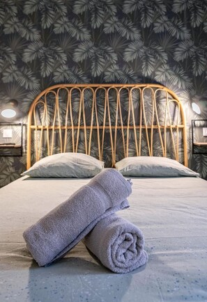 A bed with a wooden headboard, two pillows, and a rolled-up towel on a textured bedspread.