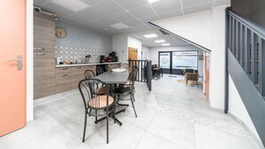 Ett modernt kök med en matplats, med ett stort bord och stolar, en klocka och en kakelbeklädd vägg bakom arbetsbänken.