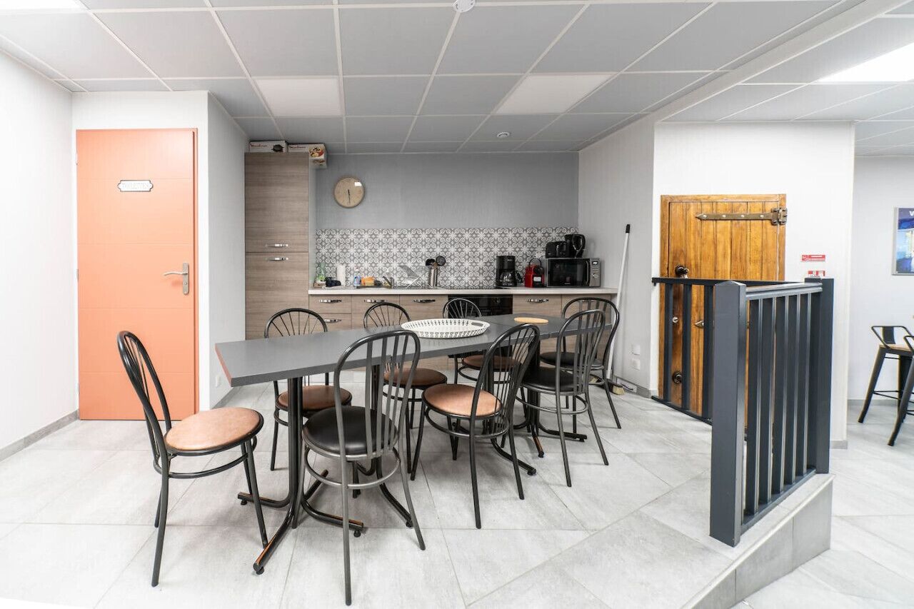 A modern kitchen with a dining area, featuring a large table with chairs, a coffee machine, and a microwave.