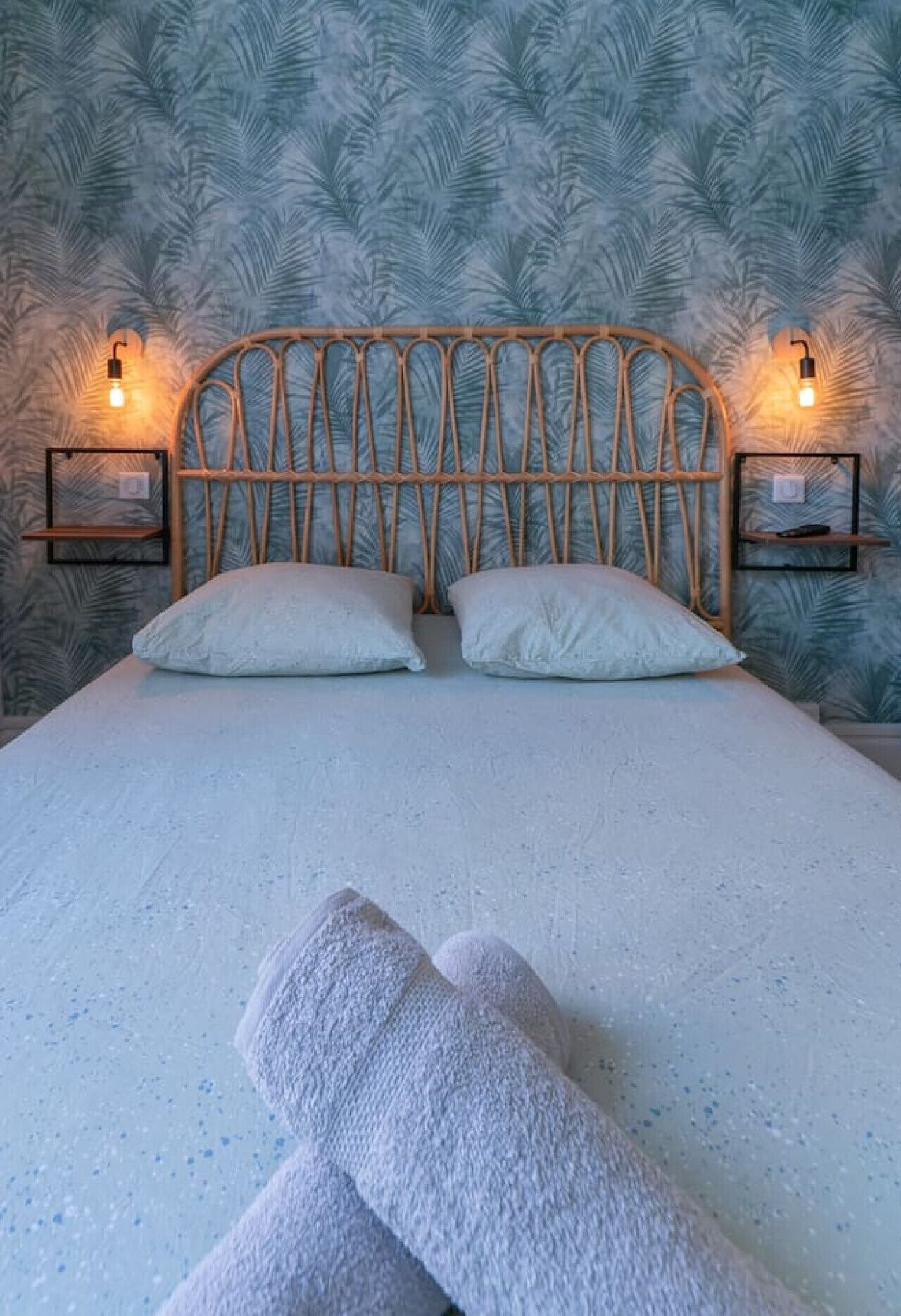 A bed with a wooden headboard, two pillows, and two bedside tables with wall-mounted lamps.