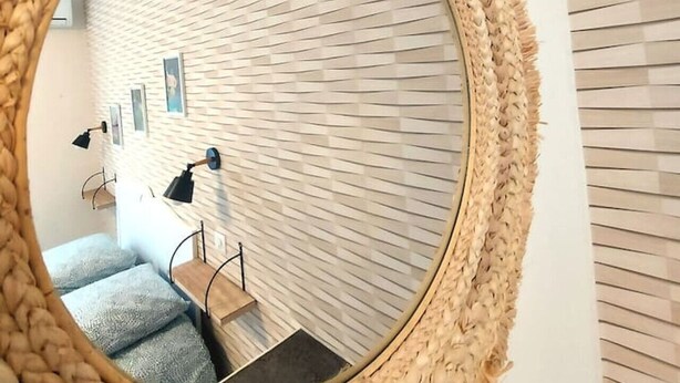 A round mirror with a textured frame, reflecting a staircase and a wall with a woven pattern. - Grande Maison de ville design avec parking gratuit (Gannat)