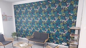 A room with wicker furniture, a bookshelf, and a floral-patterned wall. - Grande Maison de ville design avec parking gratuit (Gannat)