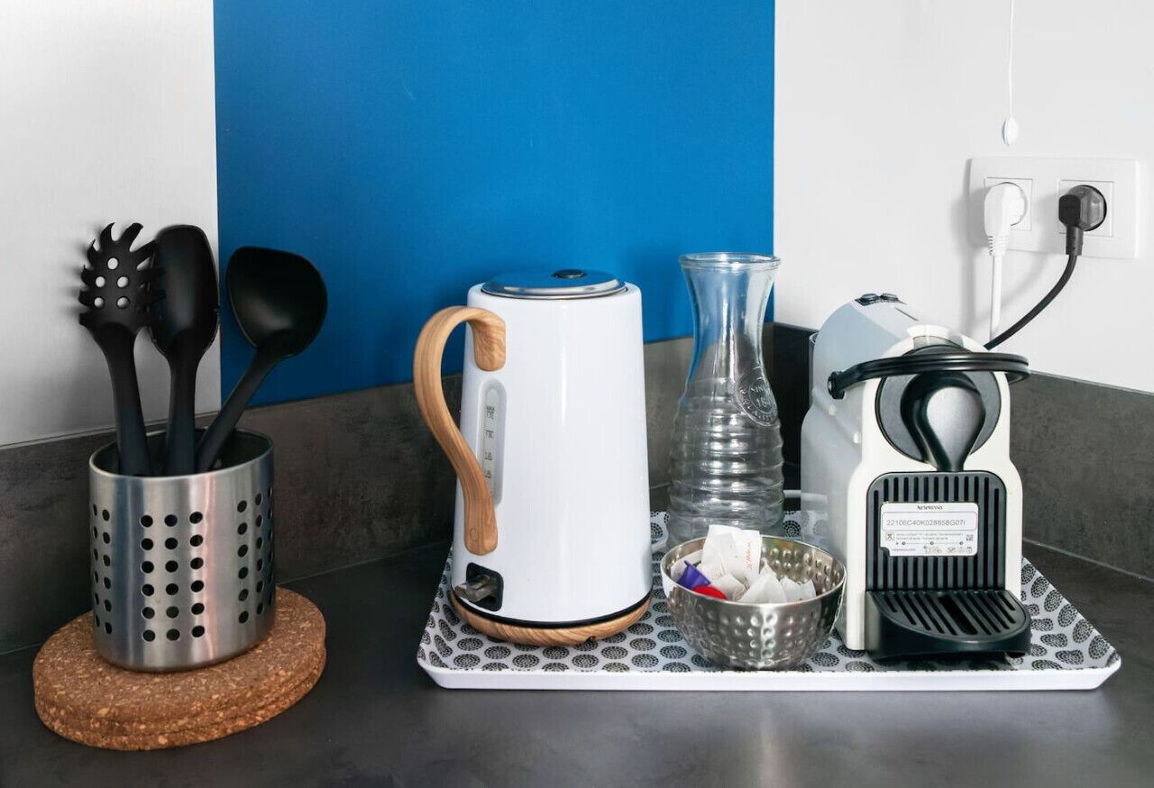 Un plan de travail de cuisine avec une machine à café, une bouilloire, un vase en verre et des ustensiles disposés sur un plateau.