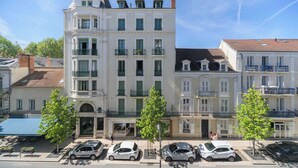 A multi-story building with a central entrance, balconies, and a parking area with cars. - Superbe loft climatisé dans immeuble classé (Vichy)