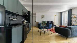 A modern kitchen with dark cabinets, a dining area with blue chairs, and a living room with a sofa. - Superbe loft climatisé dans immeuble classé (Vichy)