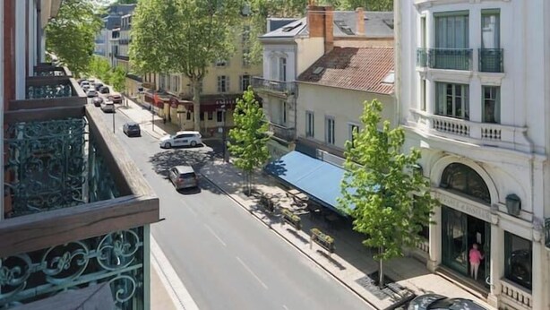 A street view with buildings, a clear sky, and parked cars. - Superbe loft climatisé dans immeuble classé (Vichy)