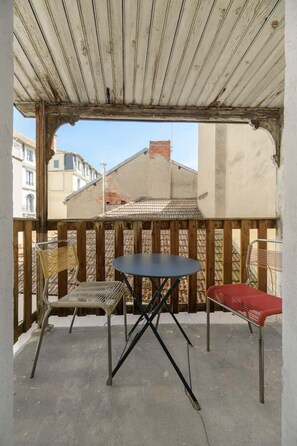 Un balcon avec une balustrade en bois, une table ronde et deux chaises.