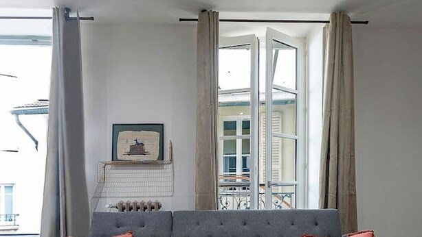 Una sala de estar moderna con un sofá seccional gris, una mesa de centro de mármol y vistas al exterior a través de grandes ventanales.