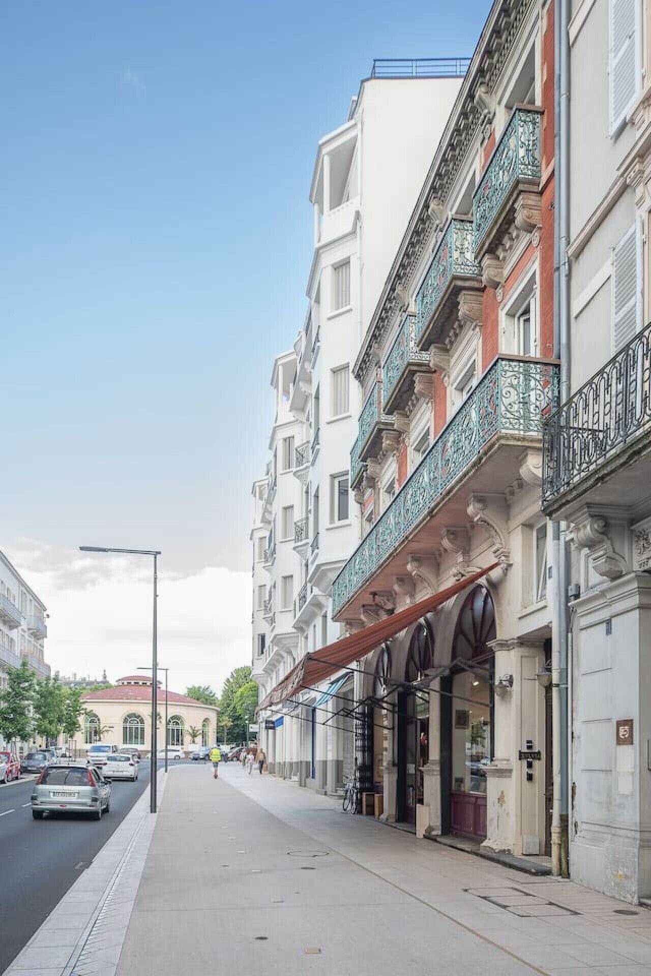 A street view with a row of multi-story buildings, some with balconies and storefronts.
