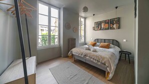 Une chambre à coucher avec un lit, une fenêtre, un radiateur et un mur décoré d’œuvres d’art.