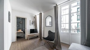 Ein modernes Wohnzimmer mit einer Couch, einem Fernseher, einem Sessel und einem Balkon mit Geländer.