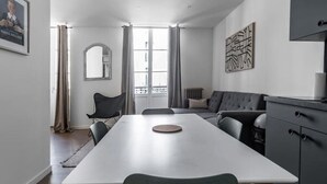 Eine moderne Küche mit einer zentralen Kochinsel, einem Essbereich mit Tisch und Stühlen sowie einem Wohnbereich mit Sofa und Fernseher.