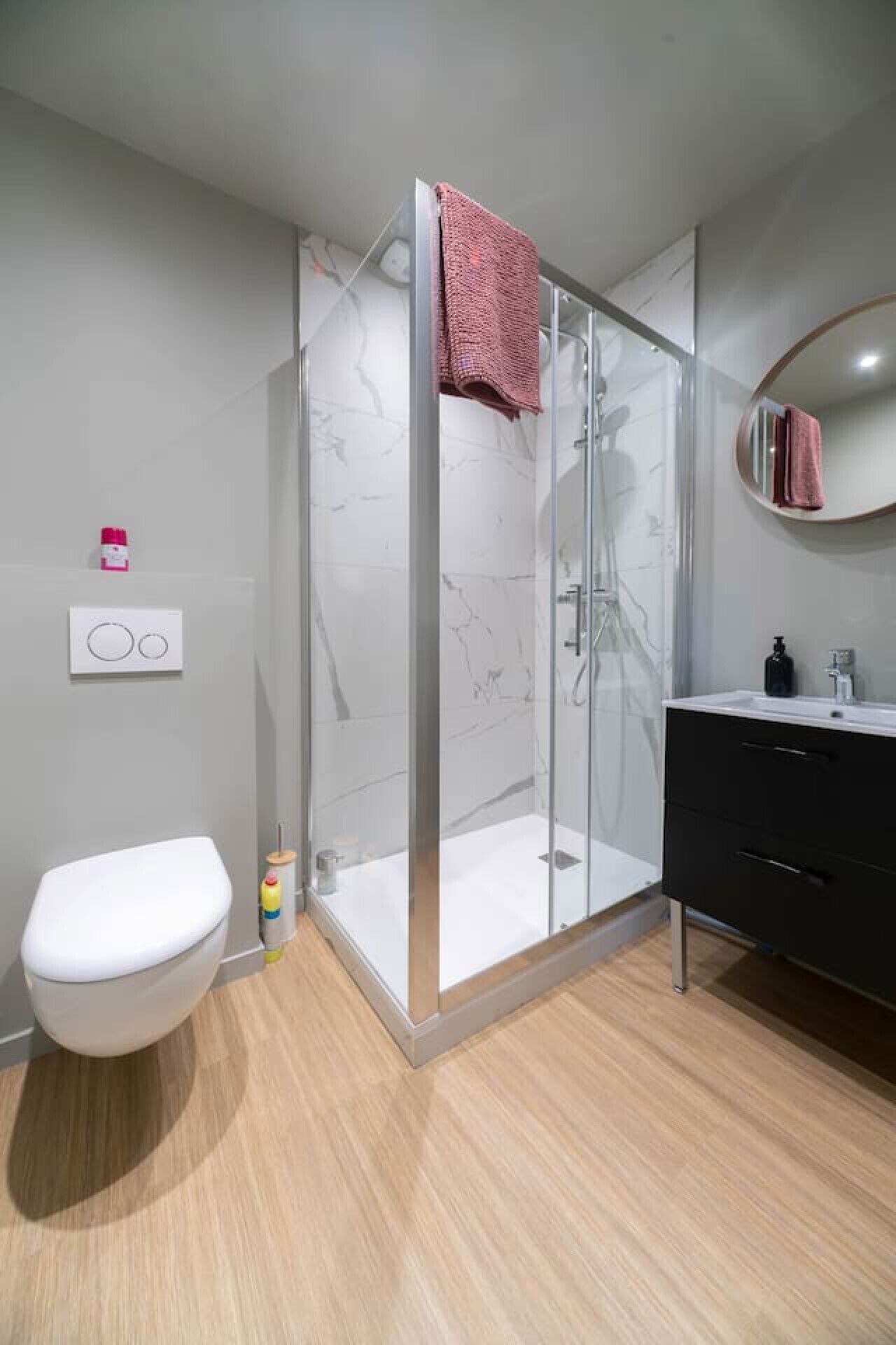 Ein modernes Badezimmer mit einer Duschkabine, einer weißen Toilette, einem schwarzen Waschtisch und einem Spiegel.