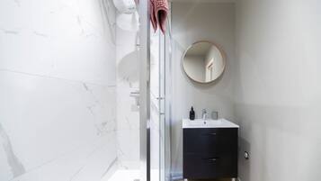 A modern bathroom with a glass shower enclosure, a round mirror, and a black vanity with a white sink.