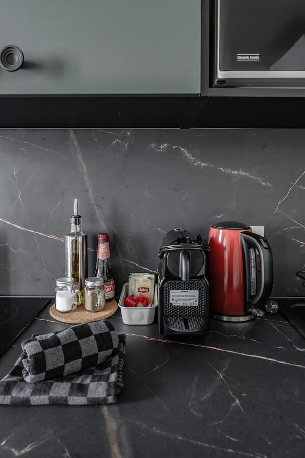 Un comptoir de cuisine avec une machine à café, une bouilloire, une bouteille et un torchon à carreaux.