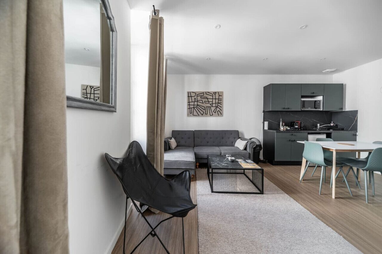 Een moderne woonkamer met een grijze bank, een zwarte stoel, een salontafel en een eethoek met een tafel en stoelen.