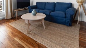 Una sala de estar moderna con un sofá azul, una mesa de centro redonda, un televisor y dos obras de arte enmarcadas en la pared.
