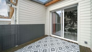 Un patio techado con piso estampado, una puerta corrediza de vidrio que da a un espacio exterior con mesa y sillas, y una cerca gris.