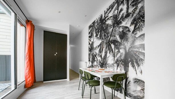 Un comedor con una mesa blanca, sillas verdes y un mural grande con palmeras.