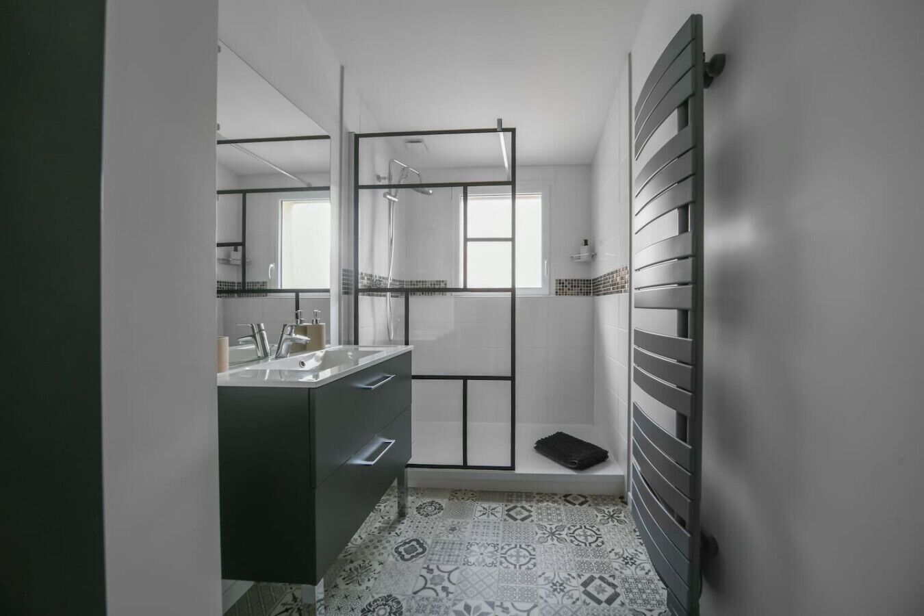 A modern bathroom with a glass shower enclosure, a sink with a mirror, and patterned floor tiles.
