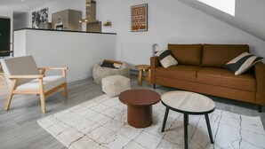 Un espacio moderno para vivir con techo estilo loft, un sofá de cuero marrón, una silla de madera y una mesa de centro redonda.