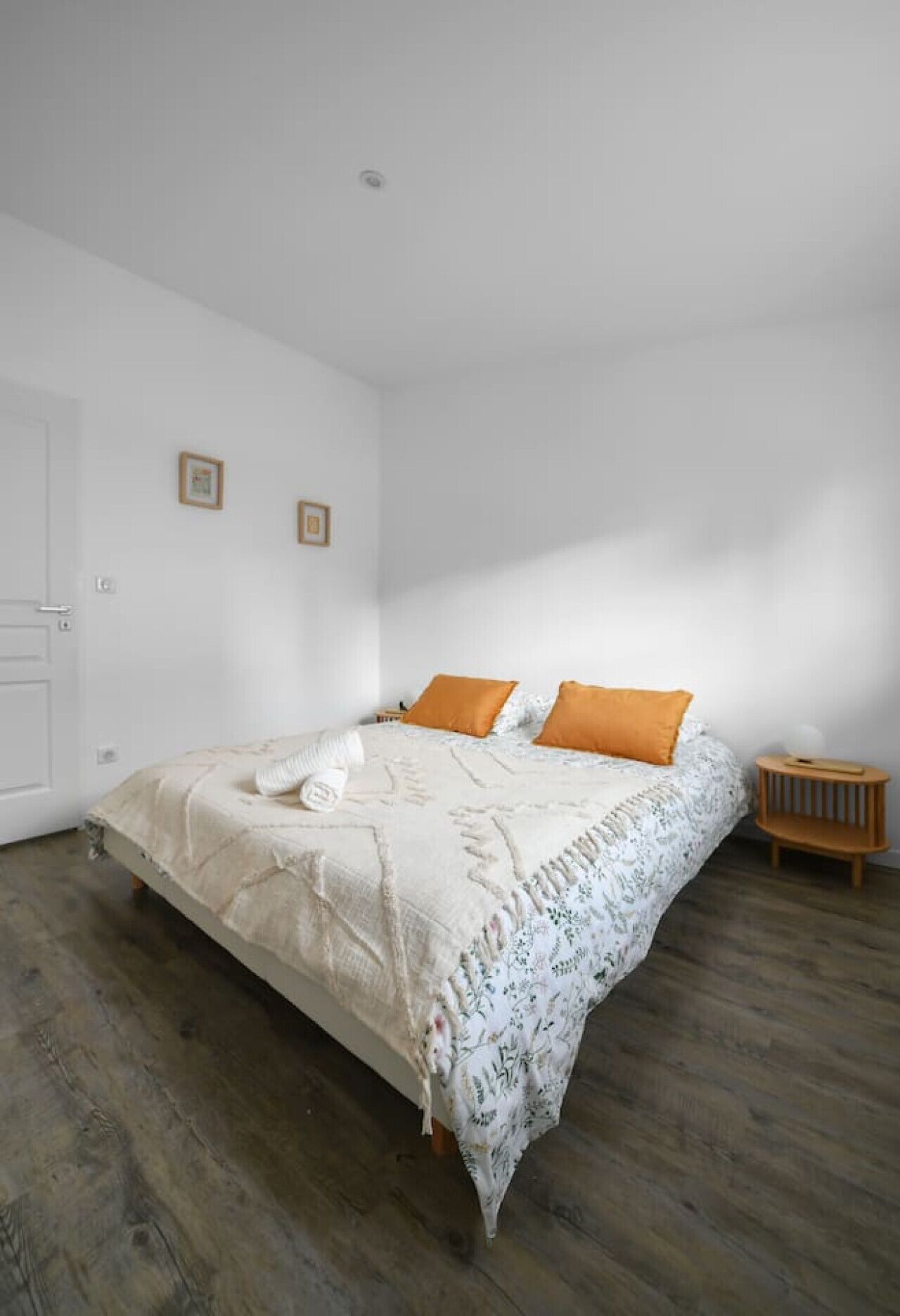 Un dormitorio con cama, dos almohadas, una mesita de noche y una puerta.
