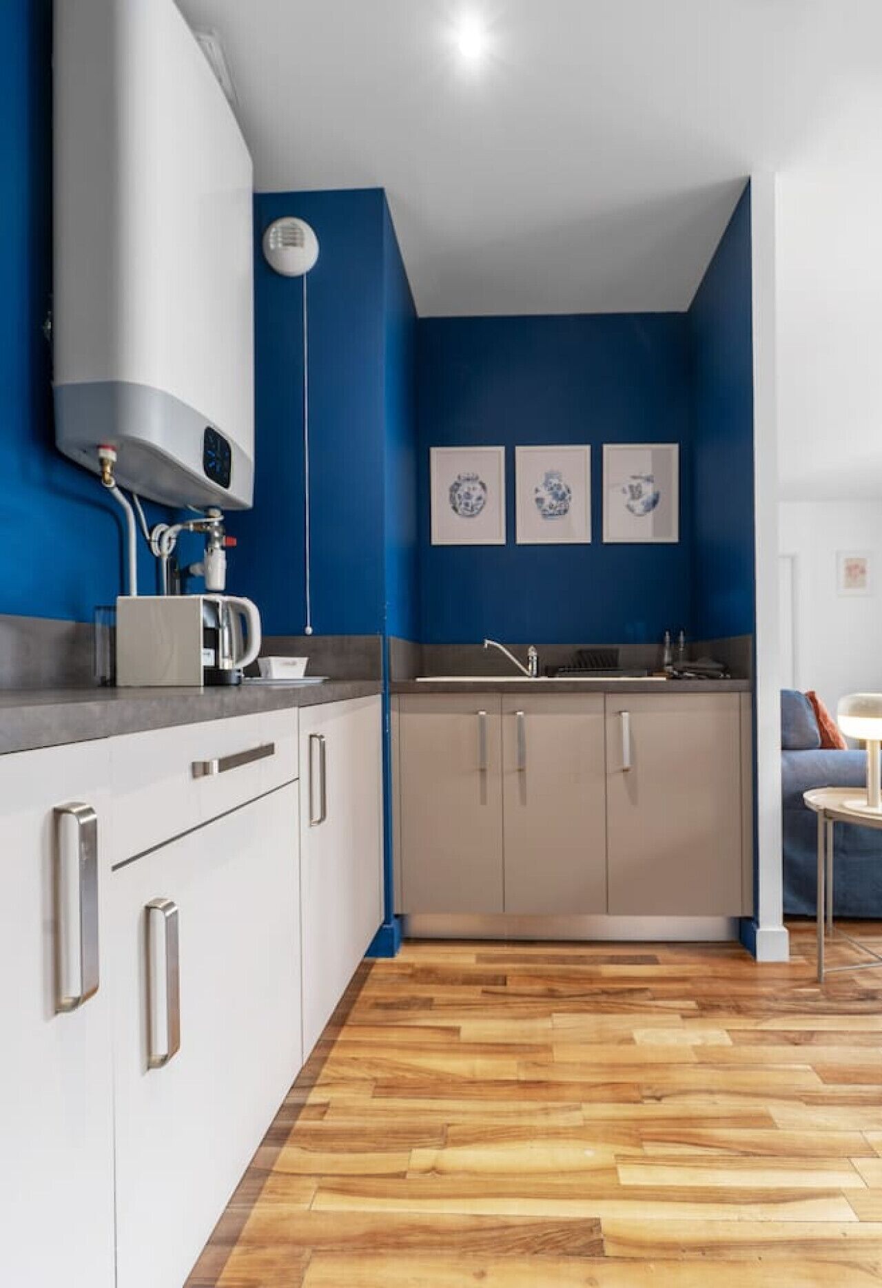 A modern kitchen with white cabinets, a blue accent wall, and a wooden floor.