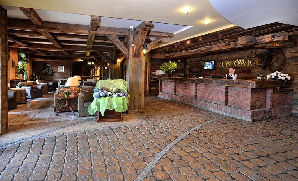 A rustic lobby with a brick reception desk, wooden beams, and a stone-tiled floor.