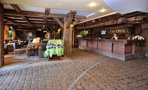 Un hall d’entrée rustique avec un comptoir d’accueil en briques, des poutres en bois et un sol carrelé en pierre.