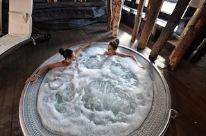 A hot tub with two people in it, surrounded by wooden pillars and a stone wall. - Ex. Best Western Hotel Zubrowka (Bialowieza)