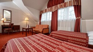 A hotel room with two beds, a desk, a chair, and a window with curtains. - Ex. Best Western Hotel Zubrowka (Bialowieza)