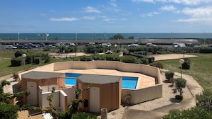 A pool area with a small building, a parking lot, and a view of the sea. - Vias Plage - Apt. vue mer 4 Pers. Climatisé Avec Piscine - REF V0823 (Vias)