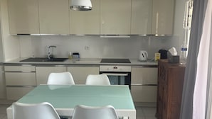 A modern kitchen with white cabinets, a stainless steel sink, a built-in oven, and a dining table with chairs. - Vias Plage - Apt. vue mer 4 Pers. Climatisé Avec Piscine - REF V0823 (Vias)