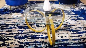 Ein Zimmer mit zwei blauen Sesseln, einem Glastisch und einer dekorativen Vasen mit Federn.