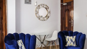 Ein Zimmer mit zwei blauen Sesseln, einem weißen Esstisch und einem gemusterten Teppich.