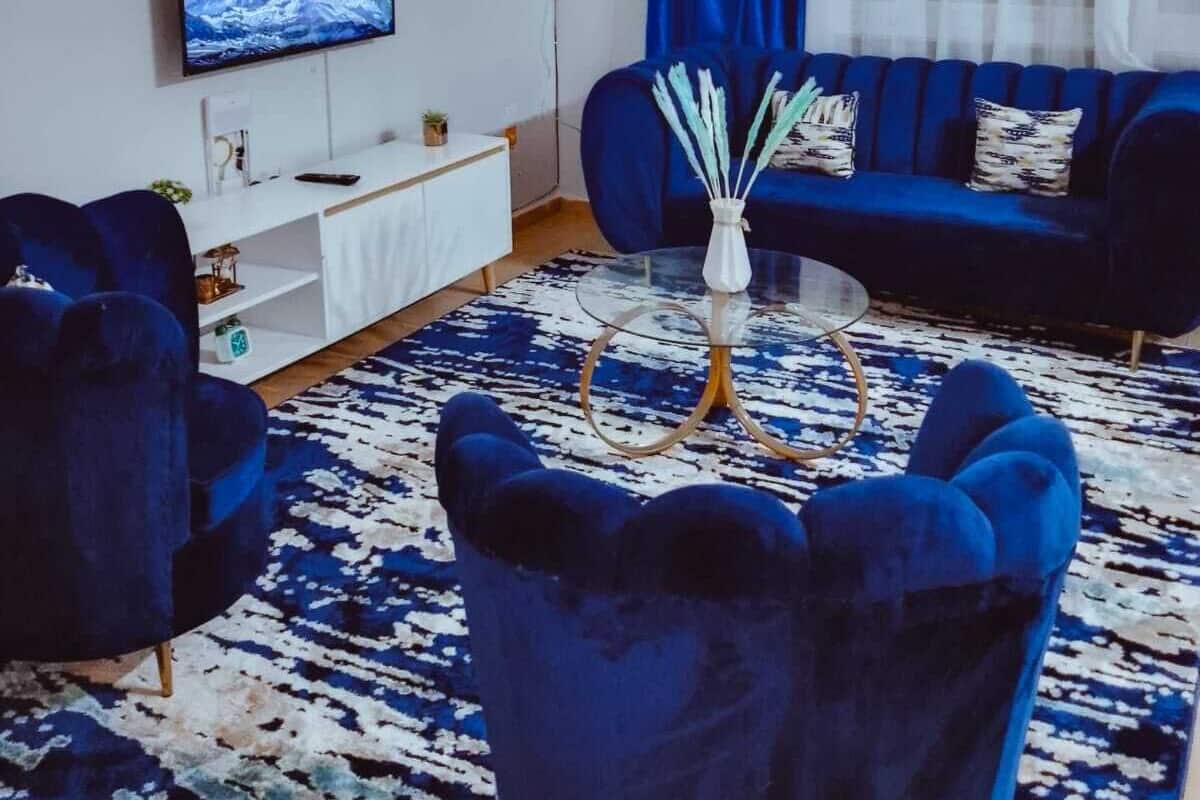 Una sala de estar moderna con un sofá azul, una mesa de centro y un televisor sobre una pared blanca.