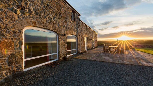 A stone building with large windows and a patio area with a table and chairs.