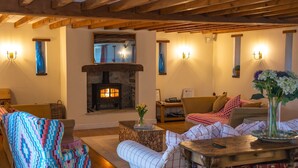 A cozy living room with a stone fireplace, wooden beams, and a comfortable seating area with patterned cushions.