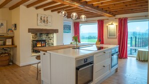 A modern kitchen with a central island, a stone fireplace, and a view of the countryside.