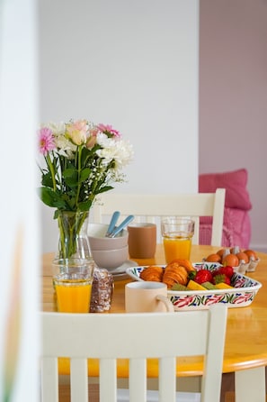 Een eettafel met een bloevas, een glas sinaasappelsap, een kom eieren en een schaal fruit.