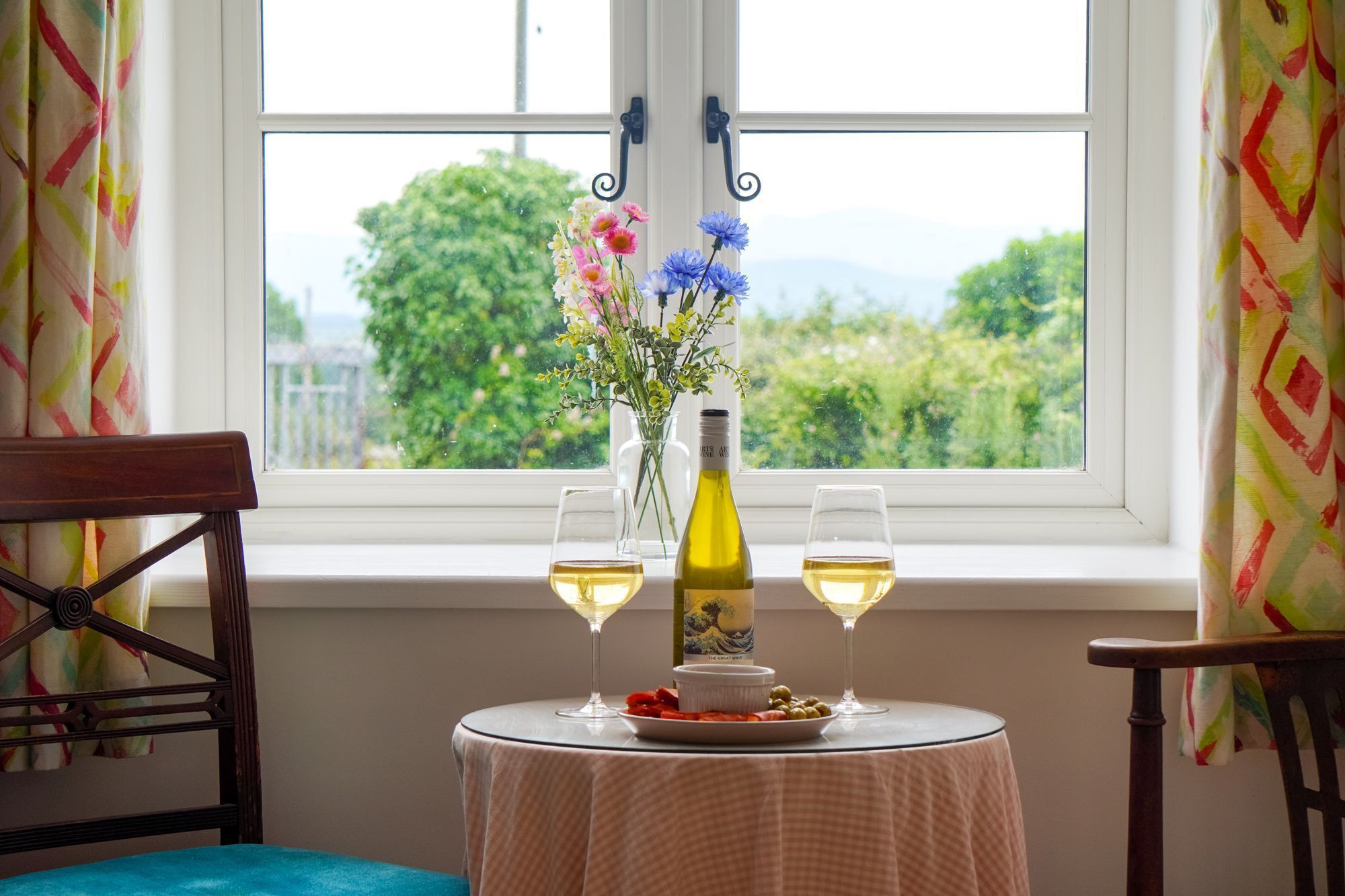 Une table avec une bouteille et deux verres de vin, une assiette avec de la nourriture et un vase rempli de fleurs.