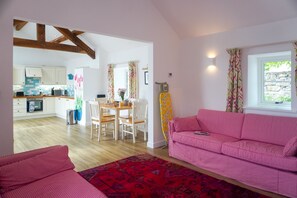 Een woonkamer met een rode sofa met patroon, een eethoek met een houten tafel en stoelen, en een keuken met witte kasten en een betegelde spatwand.