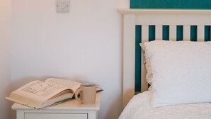 Une chambre à coucher avec un lit, une table de chevet sur laquelle se trouvent un livre et une tasse, et un luminaire fixé au mur.