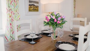 Une table à manger dressée avec des assiettes, des couverts et des verres, entourée de chaises blanches.